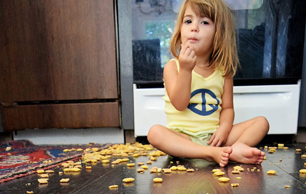 young girl sits on hardwood kitchen floor snack spilled on floor